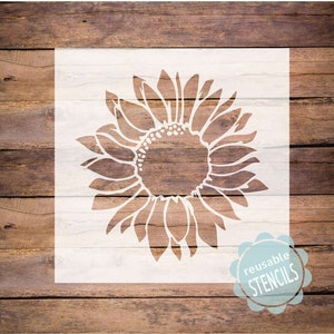 May include: A white reusable stencil of a sunflower with a detailed design. The stencil is on a wood background with the text "reusable stencils" in a circle.