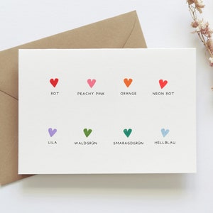 May include: A white card with colored hearts and German words for the colors. The colors are red, peachy pink, orange, neon red, lilac, forest green, emerald green, and light blue.