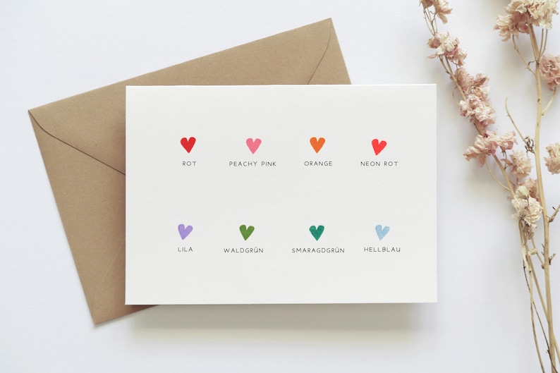 May include: A white card with colored hearts and German words for the colors. The colors are red, peachy pink, orange, neon red, lilac, forest green, emerald green, and light blue.