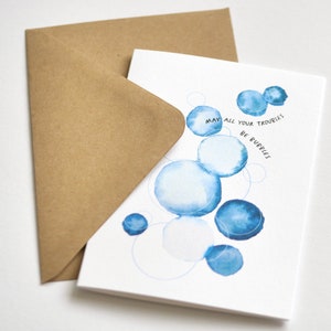 May include: A greeting card with blue watercolor bubbles and the text "May all your troubles be bubbles." The card is paired with a brown envelope. The design is simple and elegant, suitable for various occasions.
