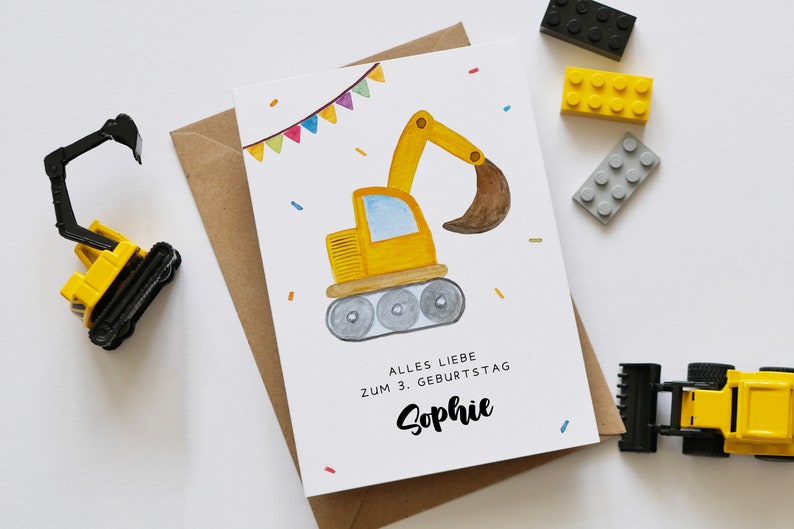 Op de afbeelding: Een gele bouwvoertuig-verjaardagskaart met een aquarel-illustratie van een graafmachine. De kaart heeft een kleurrijk lint en confetti. De tekst op de kaart luidt "Alles Liebe zum 3. Geburtstag Sophie".