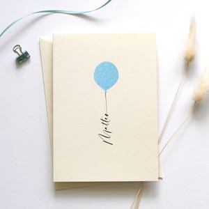 May include: A blank card with a light blue balloon and the word "little" written in black calligraphy.