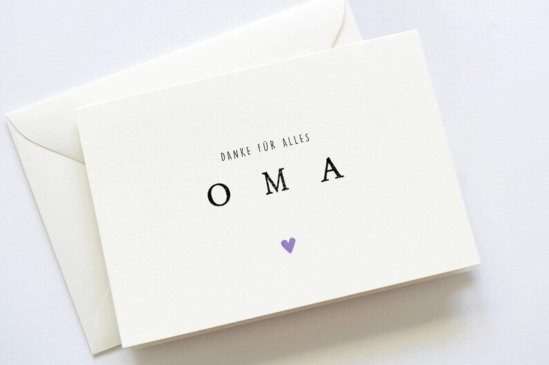 Op de afbeelding: Witte kaart met de tekst "Danke fur alles" en het woord "OMA" in grote letters. Een klein paars hartje bevindt zich onder het woord.