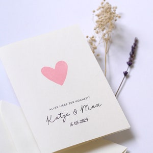 May include: A white card with a pink heart and the text "Alles Liebe zur Hochzeit Katja & Max 16.03.2024"