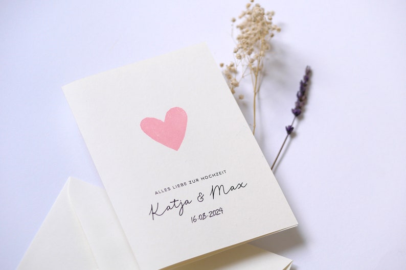 May include: A white card with a pink heart and the text "Alles Liebe zur Hochzeit Katja & Max 16.03.2024"