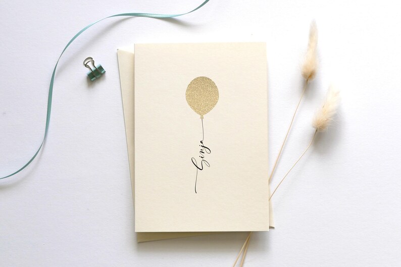 May include: A blank card with a gold glitter balloon and the word "Happy" written in black calligraphy.