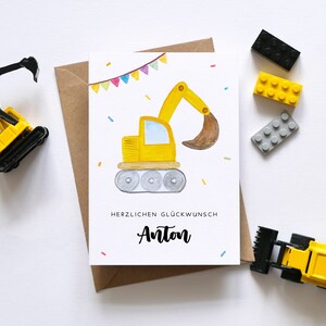 Op de afbeelding: Een gele en zwarte bouwvoertuig-verjaardagskaart met een aquarel-illustratie van een graafmachine. De kaart heeft een kleurrijk lint en confetti. De tekst op de kaart luidt "Herzlichen Gl&uuml;ckwunsch Anton".