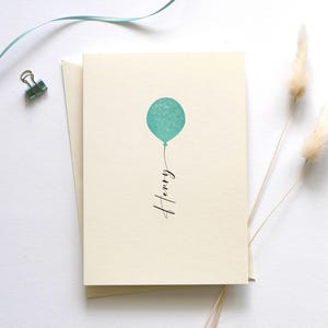 May include: A blank card with a light blue balloon and the name "Henry" written in black cursive.