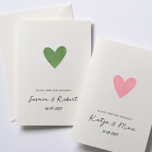 May include: Two wedding cards with a green and pink heart on each. The text on the cards reads "Alles Liebe zur Hochzeit" followed by the names of the couples and the date of their wedding. The first card says "Jasmin & Robert" and "06-07-2024". The second card says "Katja & Max" and "16-08-2024".