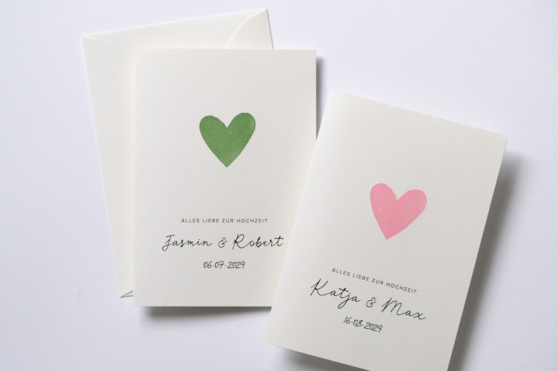 May include: Two wedding cards with a green and pink heart on each. The text on the cards reads "Alles Liebe zur Hochzeit" followed by the names of the couples and the date of their wedding. The first card says "Jasmin & Robert" and "06-07-2024". The second card says "Katja & Max" and "16-08-2024".