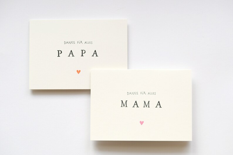 May include: Two white cards with the words "Danke fur alles" and "PAPA" on one card and "MAMA" on the other card. Each card has a small heart in a different color.