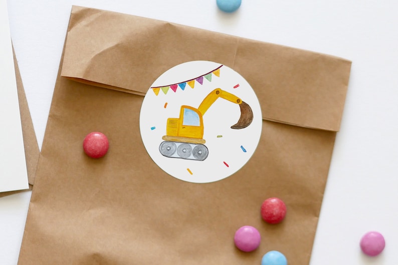 May include: A round sticker featuring a yellow construction vehicle on a white background. The vehicle has a brown scoop and is surrounded by colourful confetti and a string of flags.