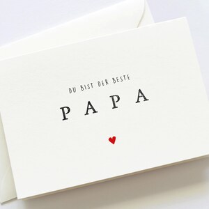 May include: White card with black text that reads "Du bist der beste Papa" with a small red heart below the text.