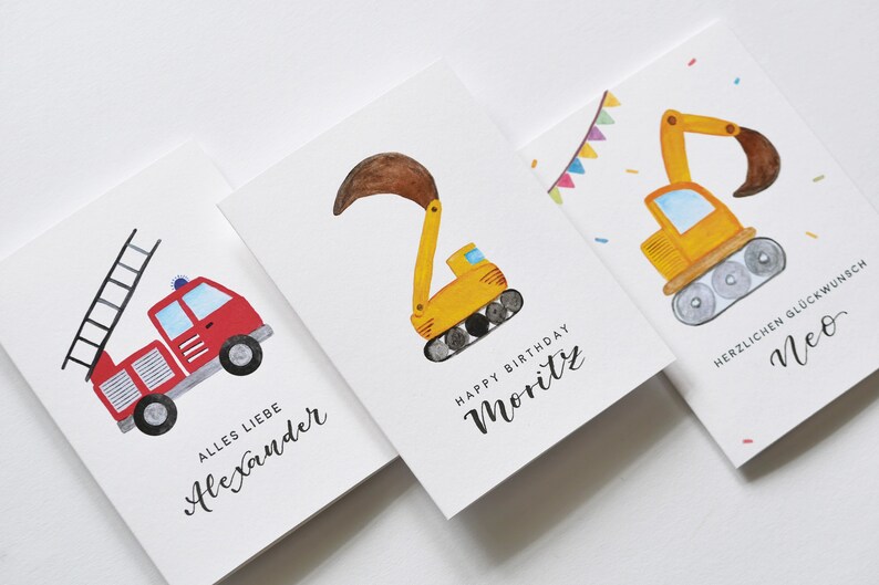 Op de afbeelding: Drie verjaardagskaarten met illustraties van bouwvoertuigen. De eerste kaart heeft een rode brandweerwagen met een ladder, de tweede kaart heeft een gele graafmachine en de derde kaart heeft een gele bulldozer. De kaarten zijn gepersonaliseerd met de namen Alexander, Moritz en Neo.