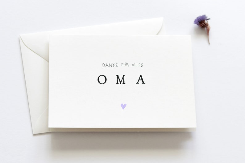 Op de afbeelding: Een witte kaart met de tekst "Danke f&uuml;r alles" en "OMA" in zwarte letters. Een klein paars hartje bevindt zich onder de tekst.