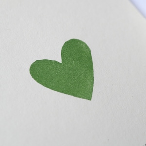 May include: A white card with a green heart in the center. The word "HOCHZEIT" is printed in black at the bottom of the card.