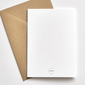 May include: A white card with a small circular logo and a brown envelope. The card is blank, and the envelope is open, with the card partially inserted. The background is white.