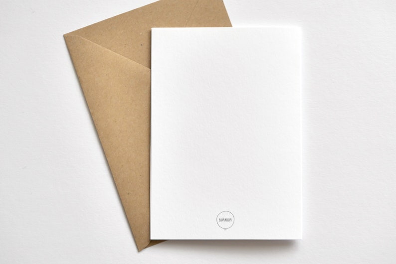 May include: A white card with a small circular logo and a brown envelope. The card is blank, and the envelope is open, with the card partially inserted. The background is white.