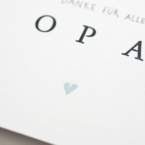 Op de afbeelding: Een witte kaart met het woord "OPA" in zwarte letters gedrukt. Het woord "Danke f&uuml;r alles" is boven het woord "OPA" gedrukt. Een klein lichtblauw hartje is onder het woord "OPA" gedrukt.