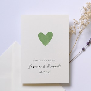 May include: A white card with a green heart and the text "Alles Liebe zur Hochzeit Jasmin & Robert 06-07-2024".