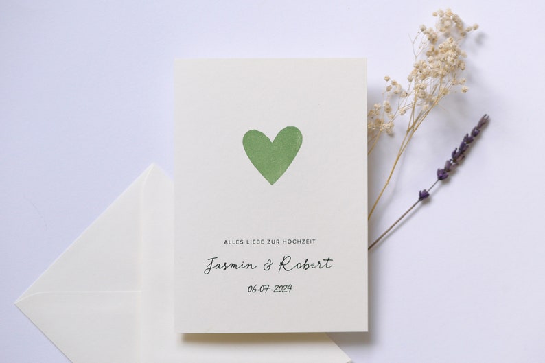 May include: A white card with a green heart and the text "Alles Liebe zur Hochzeit Jasmin & Robert 06-07-2024".
