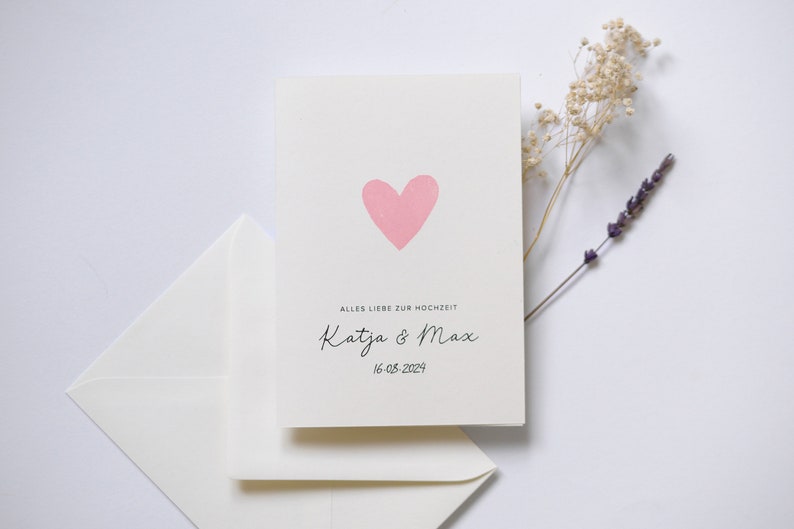 May include: A white card with a pink heart and the text "Alles Liebe zur Hochzeit Katja & Max 16.05.2024".