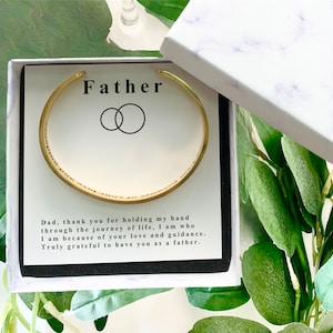May include: A gold bracelet with an inscription that reads "Dad, thank you for holding my hand through the journey of life, I am who I am because of your love and guidance. Truly grateful to have you as a father." The bracelet is in a white box with a marble pattern and the word "Father" printed on the top.
