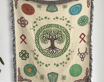May include: A cream-colored throw blanket with a woven Celtic tree of life design. The tree is surrounded by a circle of green vines and leaves. The background is beige with a variety of Celtic symbols in red, green, blue, and gold.
