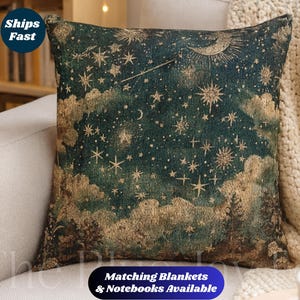 May include: Square cushion with a celestial design. It has a dark teal background with gold stars, clouds, and a crescent moon. The text "Matching Blankets & Notebooks Available" is printed on a blue banner.