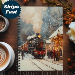 Può includere: Un dipinto ad acquerello in stile vintage di un treno a vapore che entra in un villaggio innevato. Il treno è rosso e nero con fumo bianco che esce dal camino. Il villaggio è decorato con luci di Natale e alberi coperti di neve. Il dipinto è su un taccuino a spirale con le parole "The Blue Jay Flies" stampate in basso.