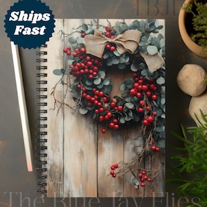 May include: Spiral-bound notebook with a rustic wreath design. The wreath features red berries, green leaves, and a burlap bow set against a wooden backdrop. The notebook has the text "The Blue Jay Flies" at the bottom. A pencil is on the side.