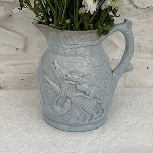 Könnte beinhalten: Eine hellblaue Keramikkanne mit einem Reliefdesign eines Wolfes, der zum Mond heult. Die Kanne hat einen rustikalen, baumartigen Griff.