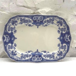 Puede incluir: Bandeja de servir rectangular antigua con centro crema y borde floral azul. El diseño azul presenta flores y follaje, creando una estética clásica y vintage. La bandeja tiene un borde festoneado.