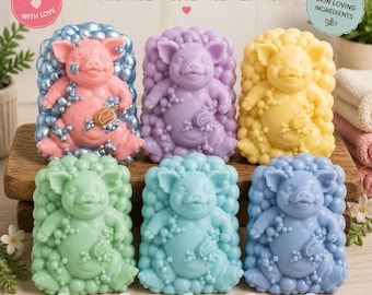 May include: Six rectangular bars of soap, each featuring a molded pig figure surrounded by bubbles. The soaps are colored pink, purple, yellow, light green, teal, and blue. Text on the image includes ADORABLE PIG SOAP, HANDMADE, and more.