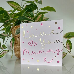 May include: A pink and gold card with the text "love you mummy x" and gold stars on a white background.