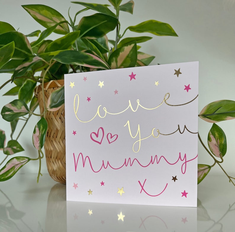 May include: A pink and gold card with the text "love you mummy x" and gold stars on a white background.