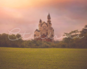 May include: A blurry image of a castle in the distance with a field of green grass in the foreground. The sky is a soft pink and orange color.