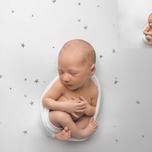 May include: A newborn baby is swaddled in a white blanket and sleeping on a white background with a scattered pattern of small grey stars.