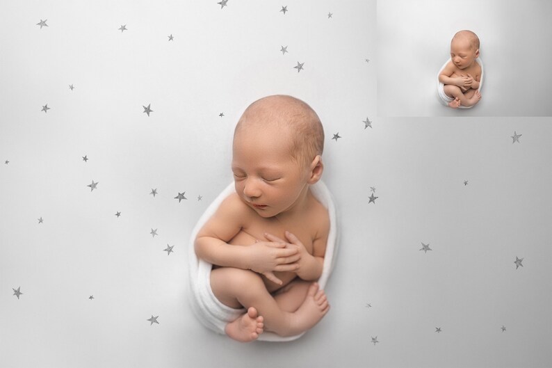 May include: A newborn baby is swaddled in a white blanket and sleeping on a white background with a scattered pattern of small grey stars.