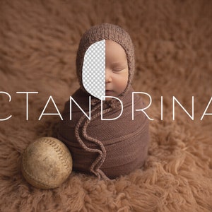 May include: A baby wrapped in a brown swaddle with a knitted hat, sleeping on a brown fuzzy surface. The baby's face is partially obscured by the hat. A baseball is in the foreground.