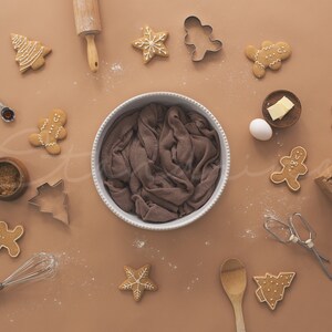 May include: A brown background with a variety of gingerbread cookies, cookie cutters, and baking supplies. There is a brown cloth in a white bowl in the center of the image.