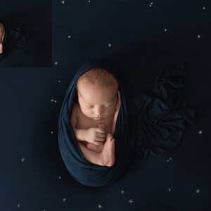 May include: A newborn baby is swaddled in a dark blue blanket and sleeping on a dark blue background with white stars.