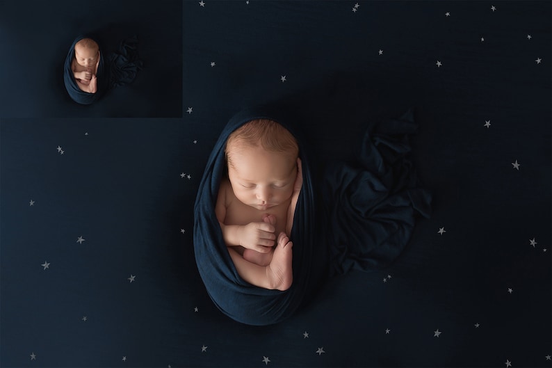 May include: A newborn baby is swaddled in a dark blue blanket and sleeping on a dark blue background with white stars.