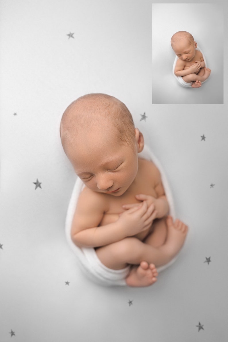 May include: A newborn baby is swaddled in a white blanket and is sleeping on a white background with grey stars.