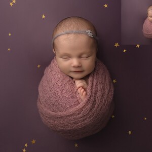 May include: A newborn baby girl is sleeping peacefully, wrapped in a soft pink swaddle. She is wearing a headband with a small, sparkly embellishment. The background is a deep purple with gold stars.