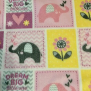 May include: A baby blanket featuring a repeating pattern of pink elephants, flowers, and the text "Dream Big little one" on a white background. The squares are in shades of pink, yellow, and purple.