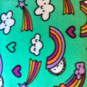 May include: A close-up of a teal fleece fabric with a repeating pattern of white clouds, purple stars with rainbow trails, purple hearts, and rainbows. The rainbows have orange, yellow, and purple stripes.