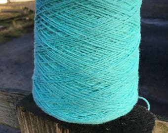 May include: A large cylindrical cone of light turquoise yarn featuring a textured, multi-ply twisted fiber construction. The yarn is wound tightly in a crisscross pattern, creating a uniform surface appearance throughout the entire spool.