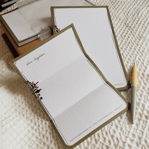 May include: Two green lined notepads with a decorative border. The top notepad has the text "Dear Neighbor." written on it. The bottom notepad has the text "Look! I am making all things new... I, these words are faithful and true - Revelation 21:5" written on it.