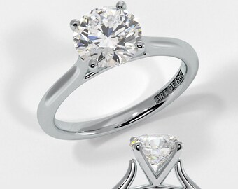 May include: A silver engagement ring with a round, clear diamond. The ring has a simple band and a four-prong setting. The inscription "ART OF FINE" is visible on the inside of the band.